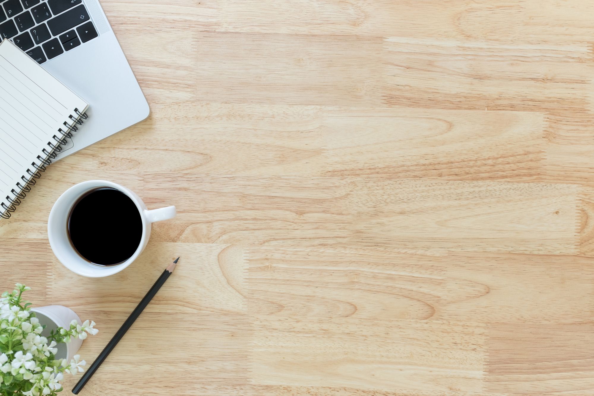 A desk with an open notebook, a cup of black coffee, a pencil and a sprig of flowers